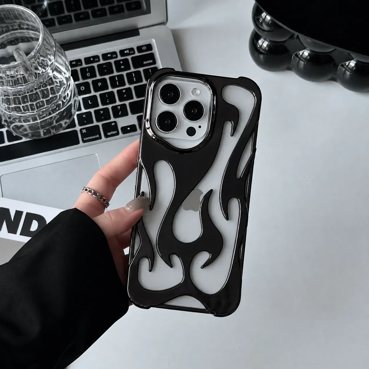 Zelpora black chrome flame iPhone case with a translucent frosted finish held in a hand over a laptop desk setup.