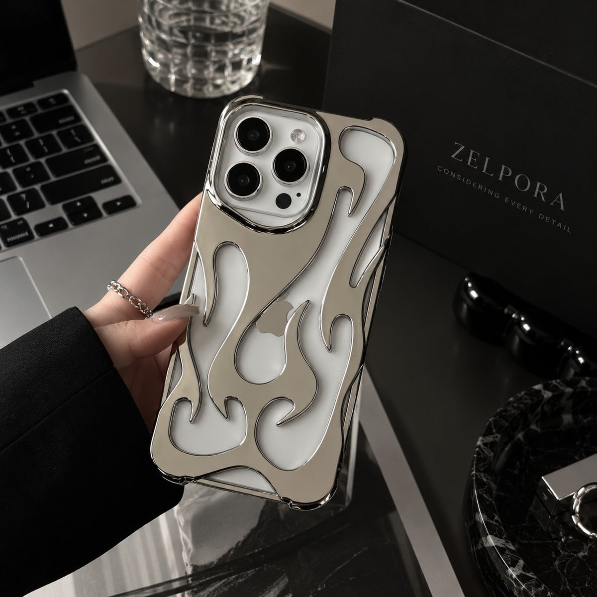 Zelpora silver chrome flame iPhone case with a translucent frosted back held in a hand on a desk