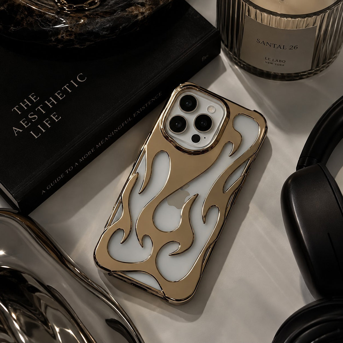 Zelpora gold chrome flame iPhone case with a frosted translucent back and raised metallic sculptural flame detailing.