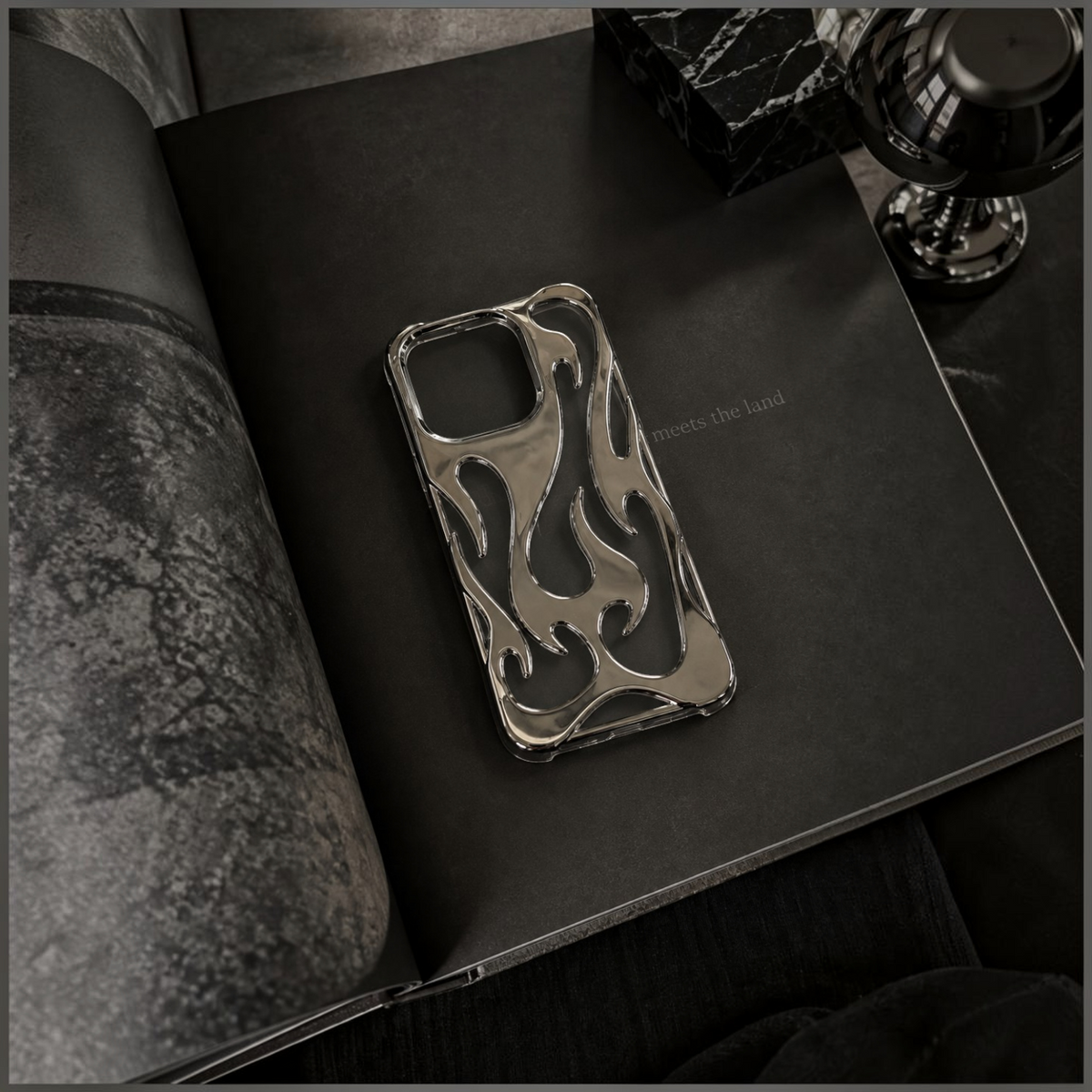 Zelpora silver chrome flame iPhone case with a sculptural, mirror-polished design on a dark background.